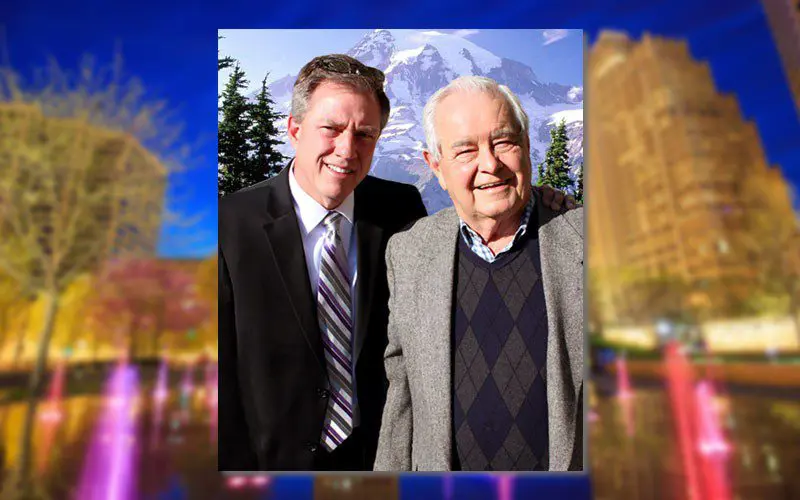 Two men standing in front of a city with mountains in the background.